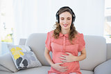 Peaceful pregnant woman relaxing listening to music sitting in living room