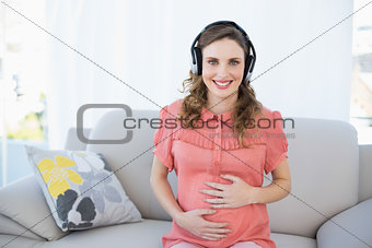 Content pregnant woman relaxing listening to music sitting on couch