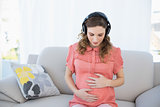 Beautiful calm pregnant woman relaxing listening to music in the living room