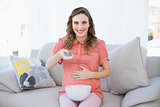 Gorgeous pregnant woman sitting on couch watching television