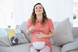 Amused pregnant woman watching television while sitting on couch in the living room