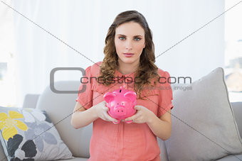 Cute pregnant woman holding a piggy bank while sitting on couch