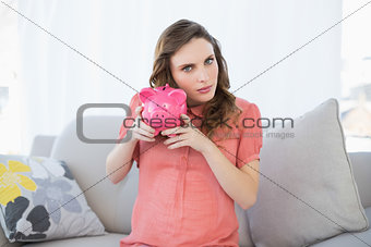 Beautiful pregnant woman shaking a piggy bank sitting on couch