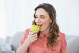 Enjoying pregnant woman eating green apple sitting on couch