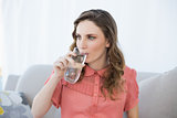 Beautiful pregnant woman drinking glass of water sitting on couch in living room