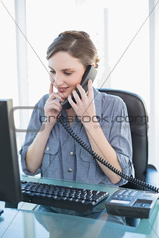 Thinking young businesswoman phoning while sitting a desk
