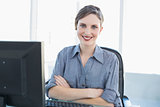 Cute young businesswoman sitting at her desk with arms crossed