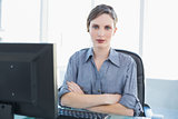 Attractive female businesswoman sitting at her desk with arms crossed