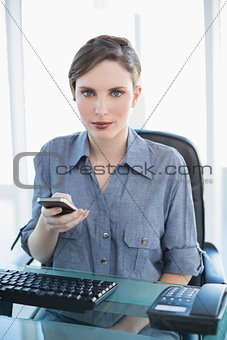 Businesswoman holding her smartphone sitting at her desk