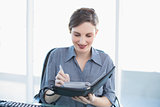 Cheerful businesswoman writing in her diary sitting at her desk