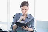 Thoughtful young businesswoman holding a diary sitting at her desk