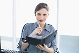 Friendly young businesswoman holding her diary sitting at her desk