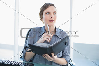 Thinking businesswoman holding her diary while sitting at her desk