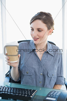 Cute businesswoman looking at disposable cup sitting at her desk
