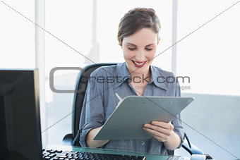 Content attractive businesswoman writing on clipboard sitting at her desk