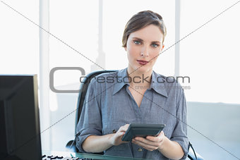 Serious attractive businesswoman holding a calculator sitting at her desk