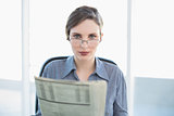 Focused businesswoman holding newspaper sitting at her desk