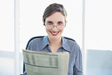 Cheerful businesswoman holding newspaper sitting at her desk
