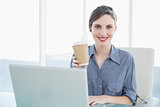 Calm beautiful businesswoman showing disposable cup while sitting at her desk