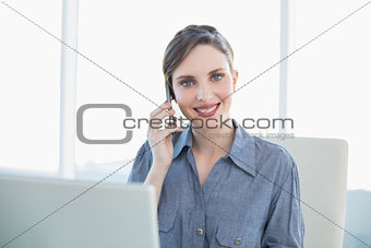 Friendly young secretary phoning with her smartphone sitting at her desk