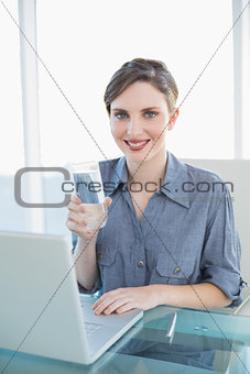 Beautiful smiling businesswoman holding a glass of water sitting at her desk