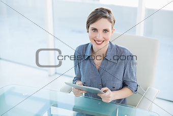 Cheerful businesswoman holding her tablet sitting at her desk