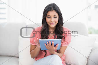 Content cute brunette sitting on couch using tablet