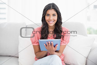 Happy cute brunette sitting on couch using tablet