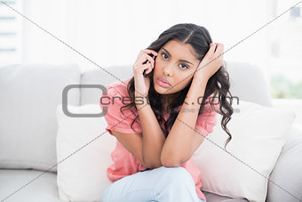 Unsmiling cute brunette sitting on couch having headache