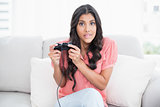 Shocked cute brunette sitting on couch holding controller