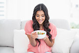 Content cute brunette sitting on couch holding salad bowl