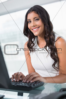 Smiling cute businesswoman sitting behind desk at computer