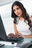 Serious cute businesswoman sitting behind desk at computer