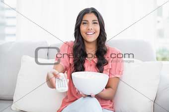 Happy cute brunette sitting on couch holding popcorn bowl