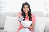 Smiling cute brunette sitting on couch holding popcorn bowl