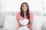 Cheerful cute brunette sitting on couch holding popcorn bowl