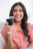 Pleased cute brunette sitting on couch holding wine glass