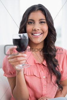 Pleased cute brunette sitting on couch holding wine glass
