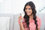 Smiling cute brunette sitting on couch holding white wine glass