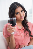 Smiling cute brunette sitting on couch holding wine glass