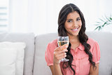 Happy cute brunette sitting on couch holding white wine glass