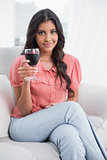 Content cute brunette sitting on couch holding wine glass