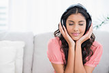 Calm cute brunette sitting on couch listening to music with closed eyes