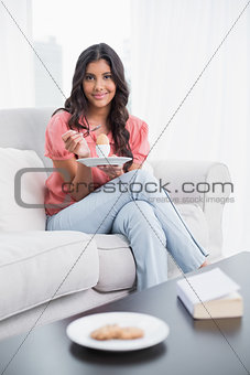 Smiling cute brunette sitting on couch holding hard boiled egg