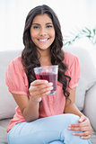 Cheerful cute brunette sitting on couch holding glass of juice