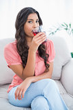 Content cute brunette sitting on couch drinking glass of juice