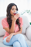 Calm cute brunette sitting on couch drinking glass of juice