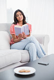Calm cute brunette sitting on couch reading