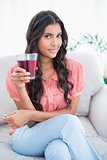 Pleased cute brunette sitting on couch holding glass of juice