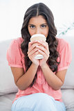 Calm cute brunette sitting on couch drinking from disposable cup